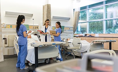 Students and a mentor reading charts over a patient bed